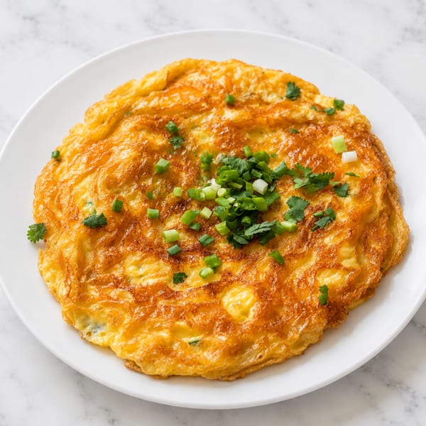 Golden-brown omelet topped with fresh green onions and cilantro on a white plate.