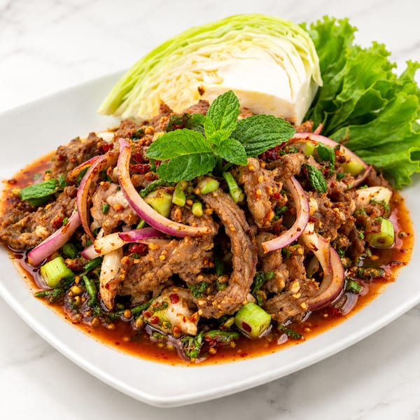 Spicy Thai beef salad with red onions, mint, and lettuce on a white plate.