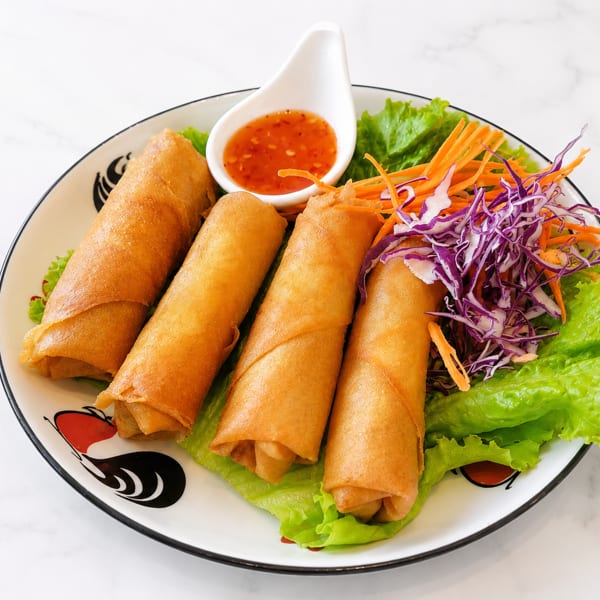 Four crispy spring rolls with lettuce, shredded carrots, purple cabbage, and dipping sauce.