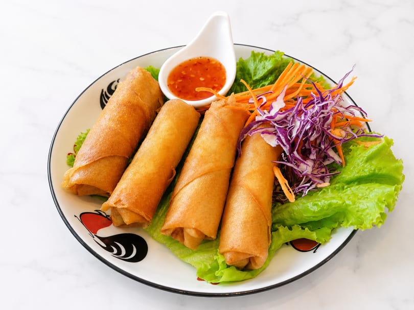 Four crispy spring rolls with lettuce, shredded carrots, purple cabbage, and dipping sauce.