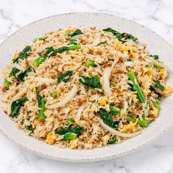 Fried rice with green vegetables, scrambled egg, and sliced onions on a white plate.