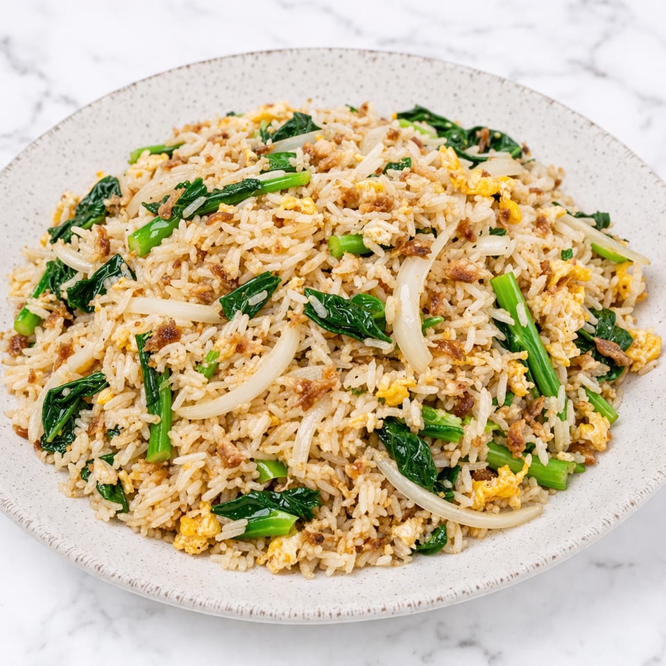 Fried rice with green vegetables, scrambled egg, and sliced onions on a white plate.