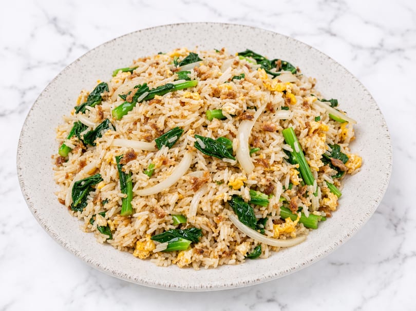 Fried rice with green vegetables, scrambled egg, and sliced onions on a white plate.